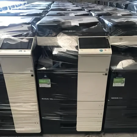 Off lease copiers on a warehouse floor, several still in their delivery wrapping.